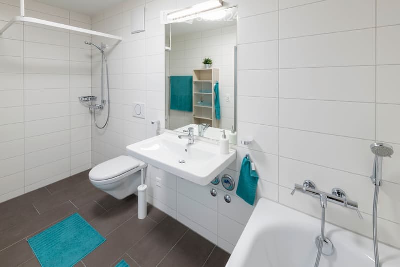 White tiles, white sink, silver shower, showerhead, bathtub, toilet, towel rack, floor mat