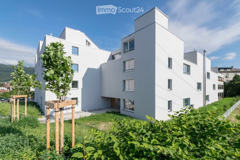 white modern multi-story building, several windows, ground level covered with greenery, two trees planted in front