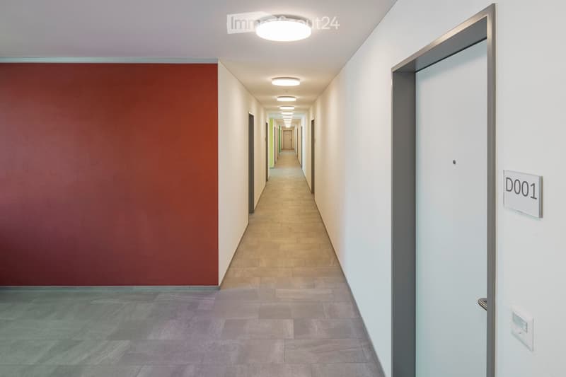 corridor with red wall, white walls, grey floor, white ceiling, and ceiling lights