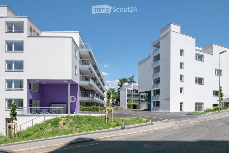 Modern apartment buildings, white walls, glass windows, multiple balconies, landscaped area