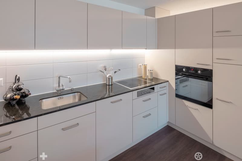 modern kitchen with white cabinets, granite countertops, integrated dishwasher, electric stove, stainless steel sink, wine rack, under cabinet lighting