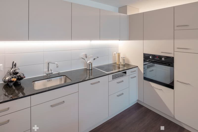 modern kitchen with white cabinets, granite countertops, integrated dishwasher, electric stove, stainless steel sink, wine rack, under cabinet lighting