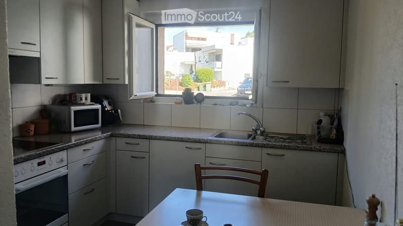 Modern kitchen with white cabinets, granite countertops, microwave, oven, sink, and a small dining area with a table and chair.