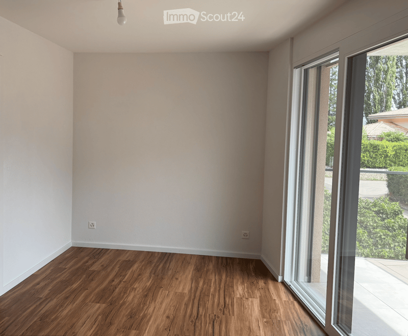 Empty room with wooden flooring, white walls, and large glass sliding doors leading to a balcony or outdoor area.