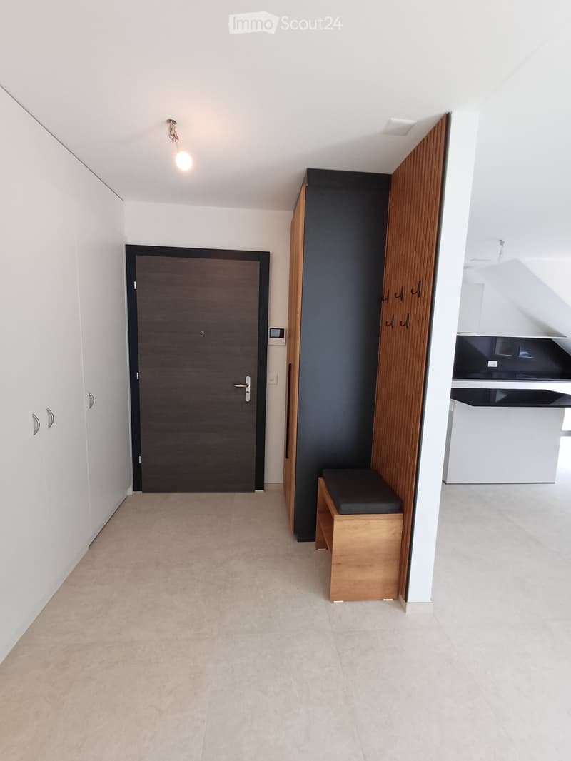 Empty hallway with beige tiled floor, white walls, a wooden bench, and a closed door.