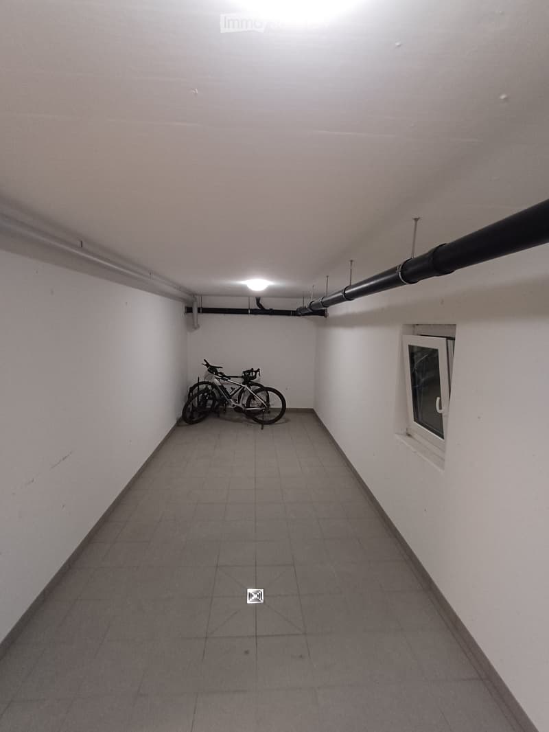 Empty hallway with tiled floor, white walls, and a small window on the right side. Two bicycles are leaning against the left wall.