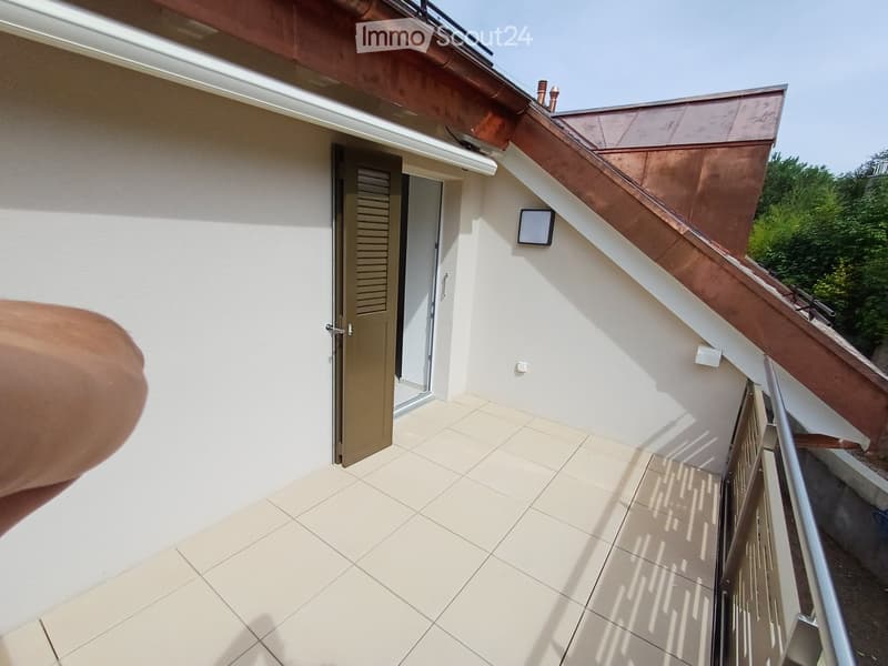 Balcony with tiled floor, white walls, metal railing, and a door leading inside.