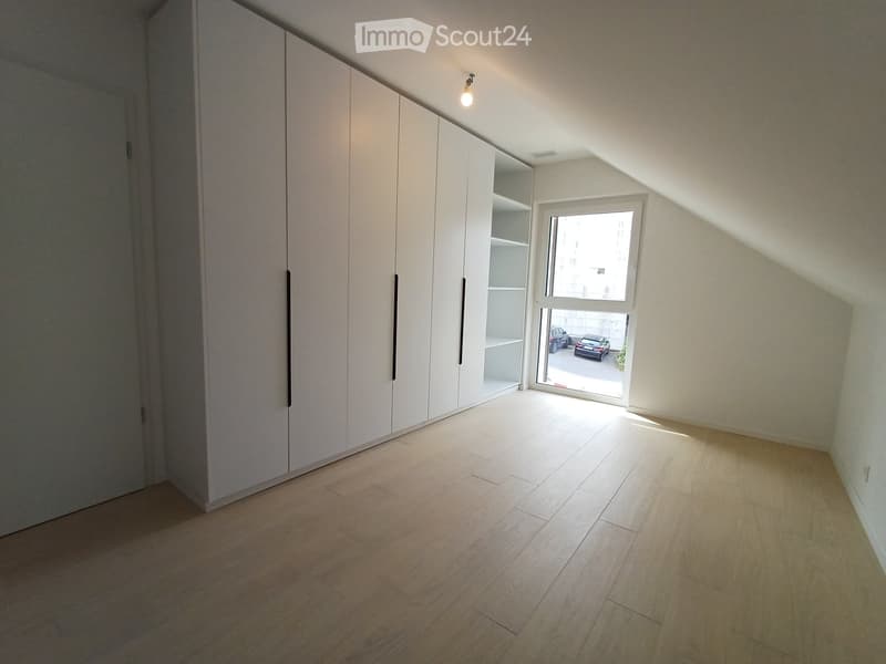 Empty room with light wooden flooring, white walls, built-in white closet units, and a large window letting in natural light.