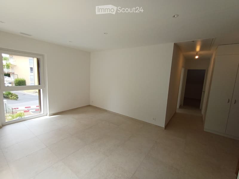 Empty room with tiled floor, white walls, large window, and a doorway leading to another space.