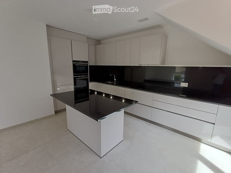 Modern kitchen with white cabinets, black countertops, and a central island. Features an oven, sink, and faucet.