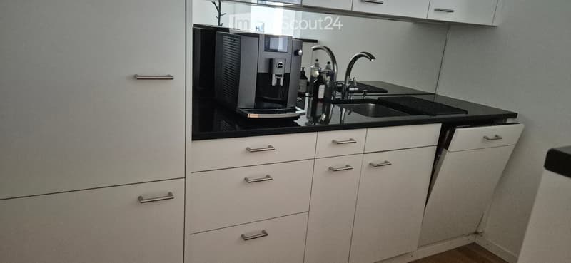 Modern kitchen with white cabinets, black countertop, coffee machine, and stainless steel faucet.