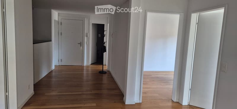 Empty hallway with wooden flooring, white walls, and multiple doors leading to different rooms.