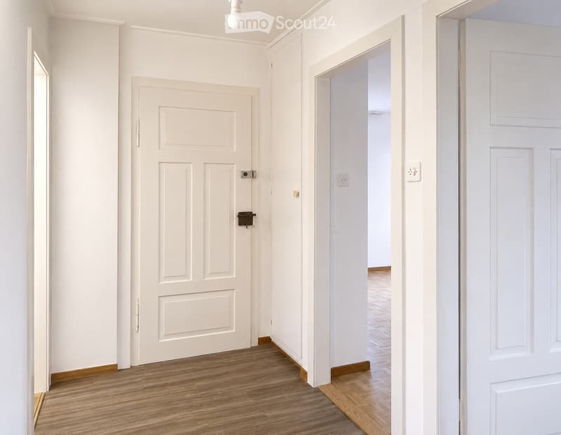 Empty hallway with wooden flooring, white walls, and multiple doors leading to other rooms.