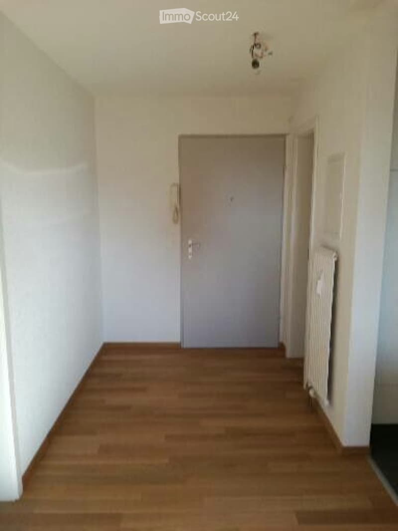 Empty hallway with wooden flooring, white walls, and a closed door at the end.