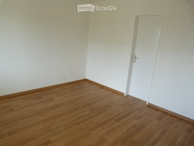 Empty room with wooden flooring and white walls, featuring a single white door.