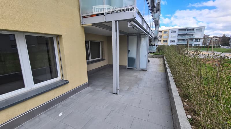 Balcony with tiled floor, glass railing, and adjacent building with large windows.