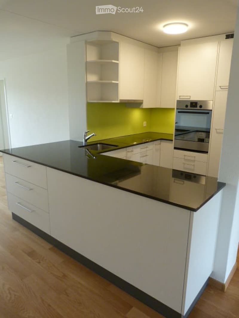 Modern kitchen with white cabinets, black countertop, stainless steel sink and faucet, and built-in oven.