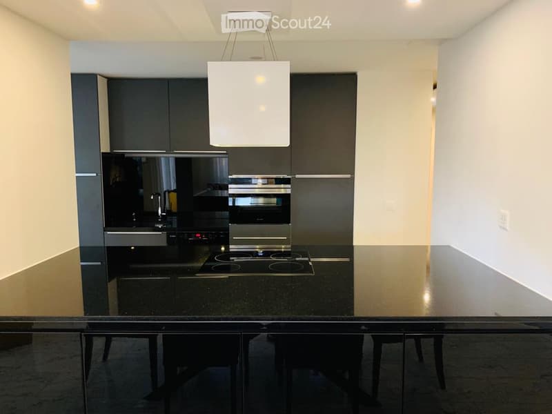 Modern kitchen with black cabinets, stainless steel appliances including a dishwasher, and a black granite countertop with a dining table and chairs