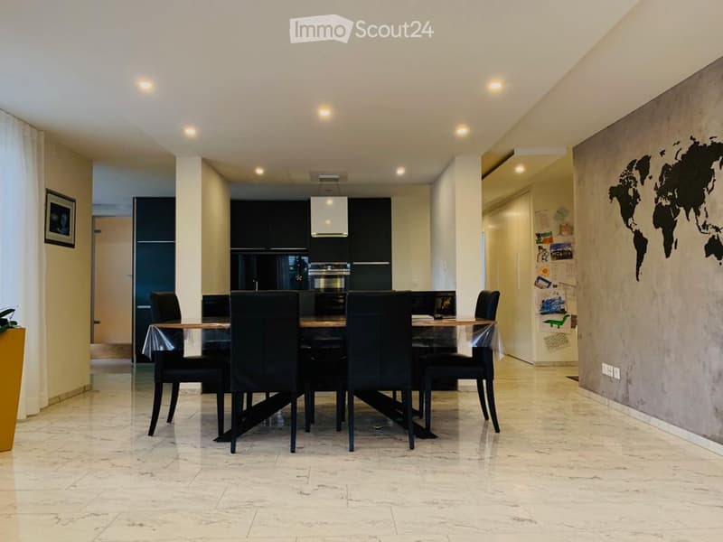 Spacious dining area with a large wooden dining table and black chairs, modern kitchen with black cabinets and appliances, world map mural on the wall, tiled flooring