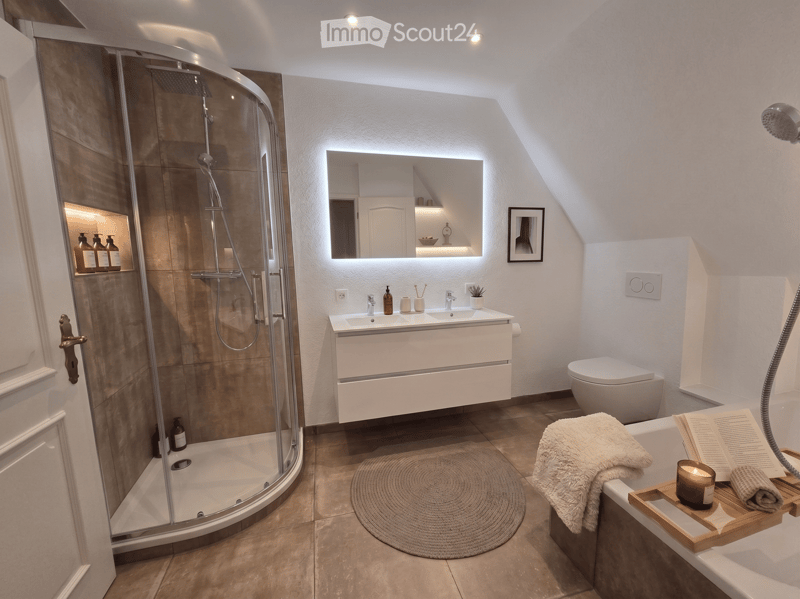 Modern bathroom with a glass-enclosed shower, double sink vanity, toilet, bathtub, and decorative items including a framed picture, towel, book, and candle on a wooden tray.