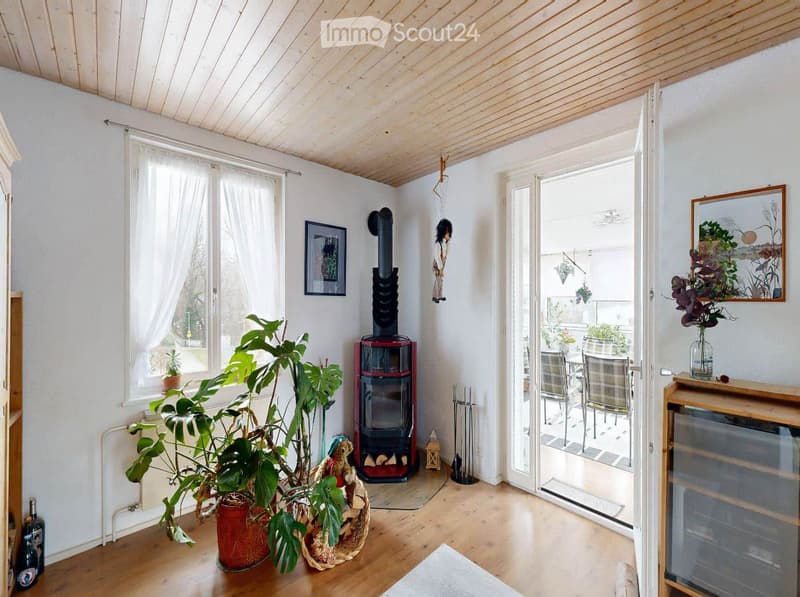 Bright living room with wooden floor, fireplace, large windows, and access to a patio with outdoor furniture.