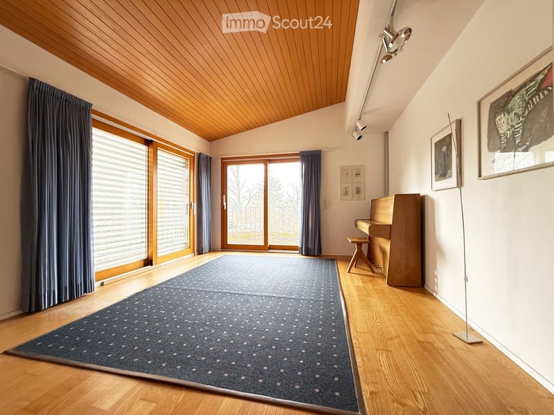 Bright living room with wooden floors, large windows, a piano, a floor lamp, and artwork on the walls.