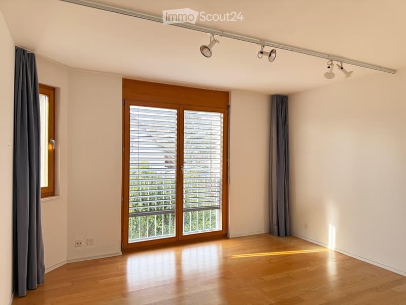 Empty room with wooden flooring, large windows, and grey curtains. No furniture or equipment present.