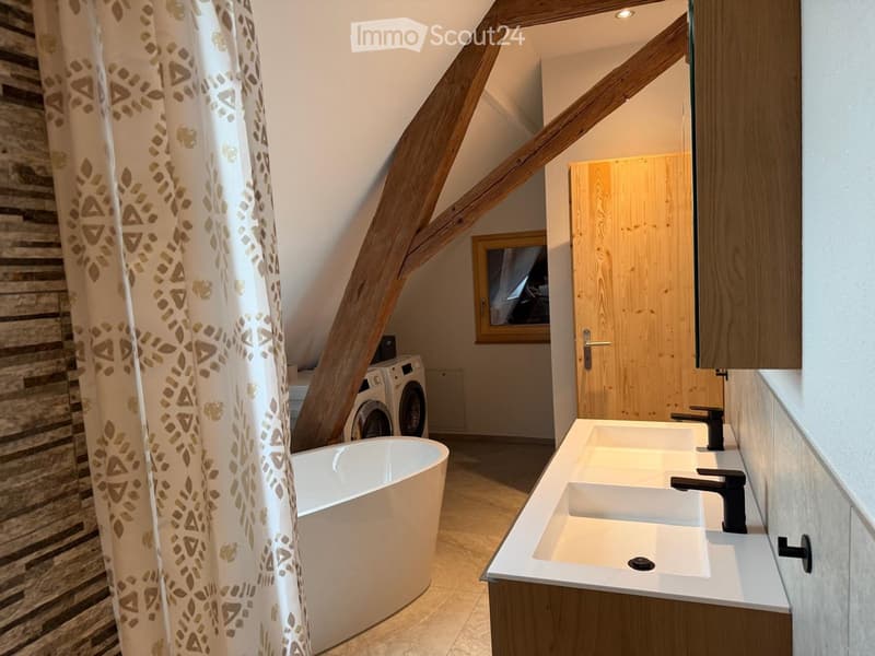 Modern bathroom with a freestanding bathtub, double sink, and a washing machine in the corner.