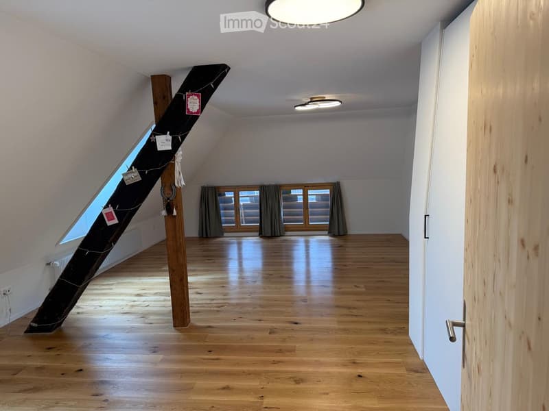 Empty attic space with wooden flooring, white walls, skylight window, and large windows with curtains.