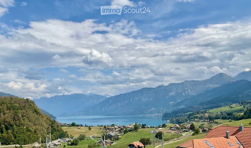 Scenic view of a lake surrounded by mountains and a small village with houses and green fields.