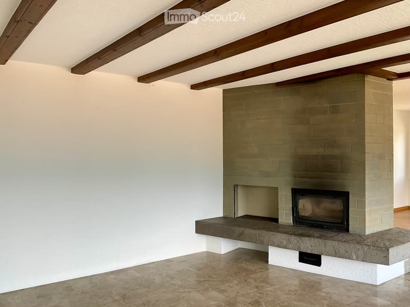 Empty room with exposed wooden beams on the ceiling, a built-in fireplace with a stone surround, and a stone bench seating area.