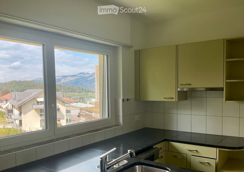 Modern kitchen with light-colored cabinets, dark countertops, and a large window offering a scenic view of the surrounding area.