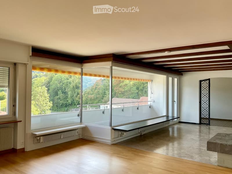 Bright, empty room with large glass windows and a balcony, wooden flooring, and modern design elements.