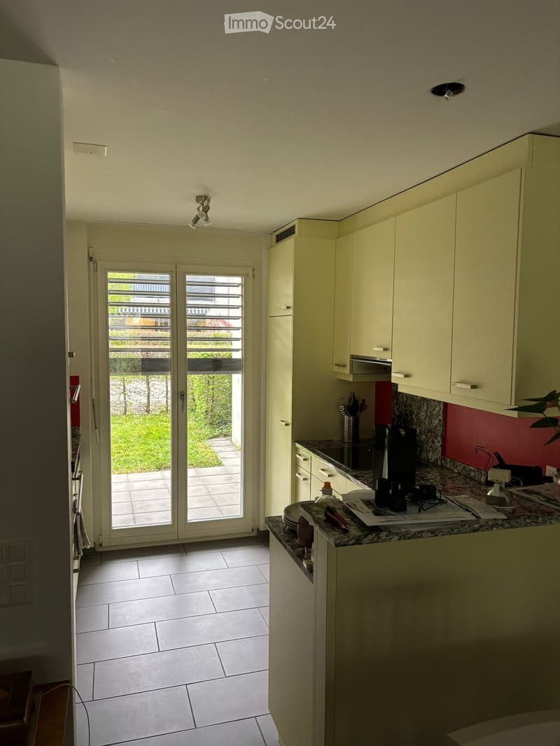 Modern kitchen with white cabinets, granite countertop, and a sliding glass door leading to a patio. Visible appliances include a microwave, refrigerator, and various small kitchen items on the counter.