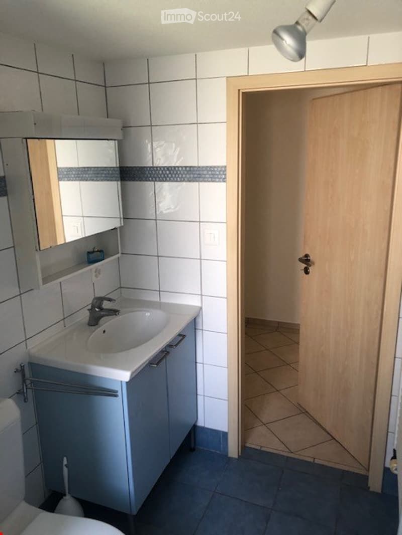 Modern bathroom with white tiled walls, a white sink with a mirror cabinet, and a wooden door leading to another room.