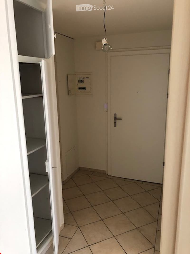 Empty room with tiled floor, white walls, a closed door, and a built-in cabinet with shelves on the left side.