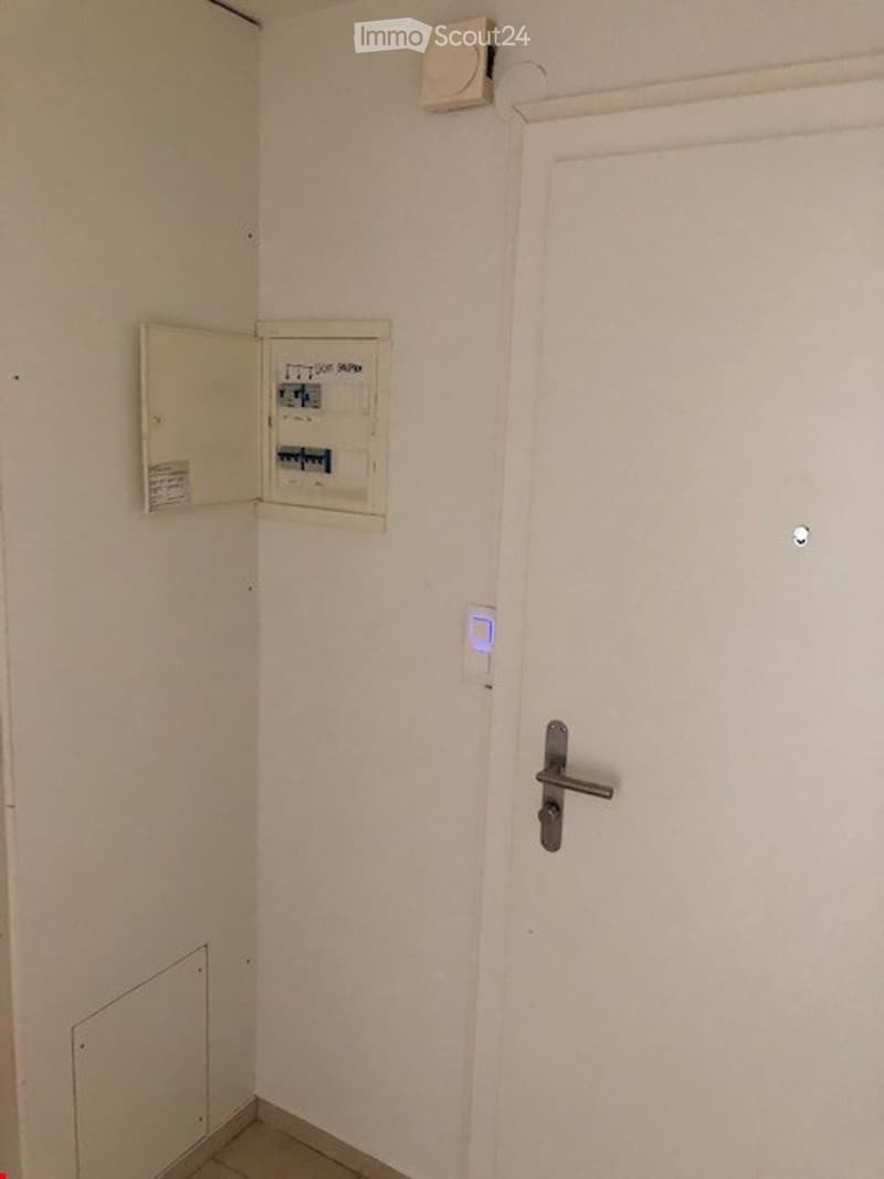 Empty utility room with a closed white door, an open electrical panel, and a light switch.