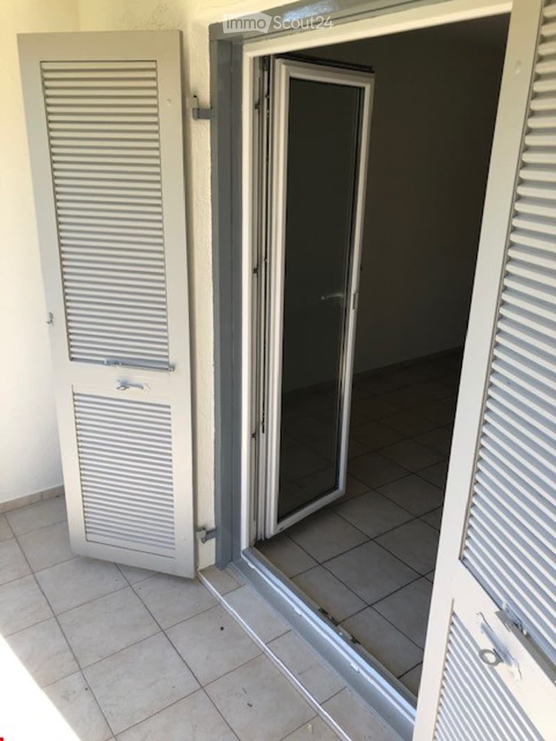 Balcony with tiled floor, white shutters, and an open sliding glass door leading to an adjacent room.
