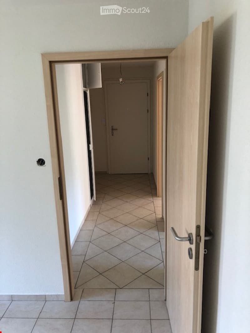 Empty hallway with tiled floor, white walls, and wooden doors.