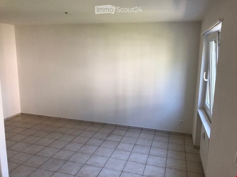Empty room with tiled floor and white walls, featuring a window with white frame and a radiator below it.