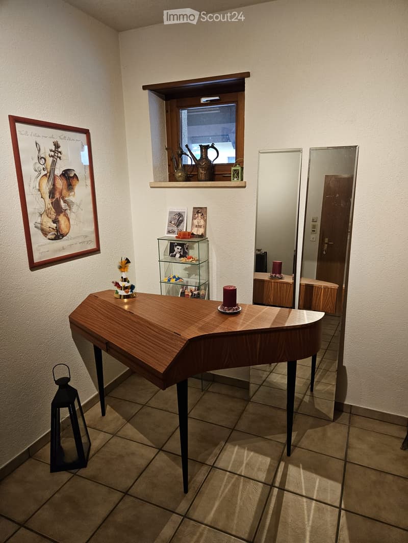 A small, well-lit room with a wooden table, a shelf with decorative items, a mirror, and a framed picture on the wall.