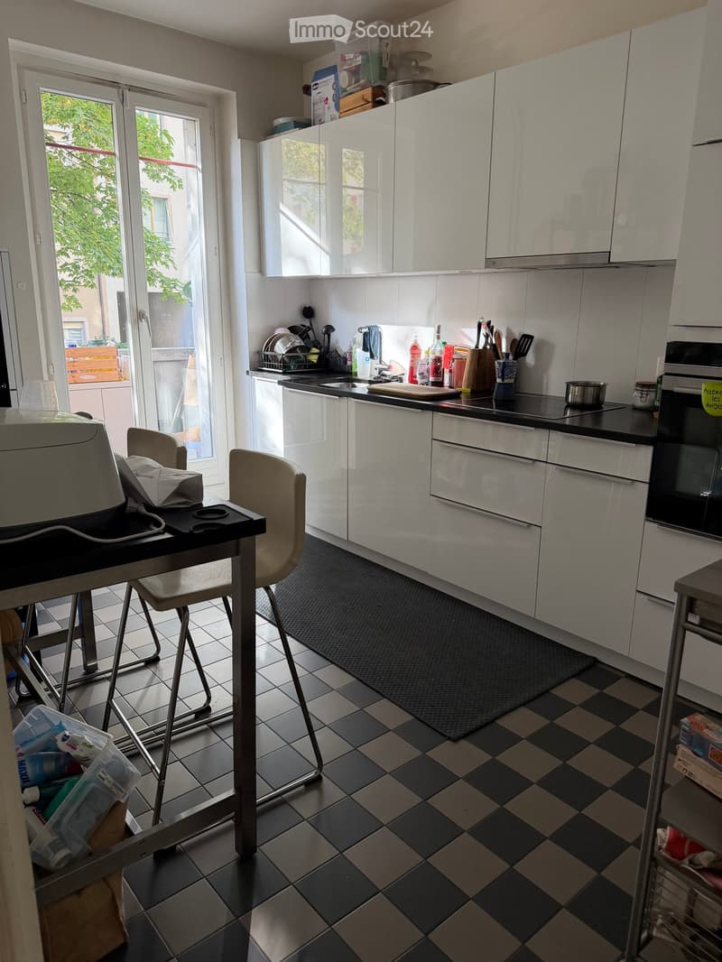Modern kitchen with white cabinets, black countertops, and a checkered floor. Includes a small table with stools, a sink, and various kitchen appliances.