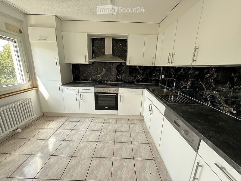 Modern kitchen with white cabinets, black countertops, and stainless steel appliances. Features a sink, oven, and radiator.