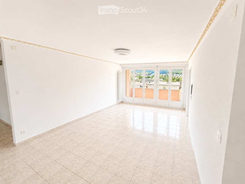 Empty room with white walls, tiled floor, and large glass doors leading to a balcony with a scenic view.