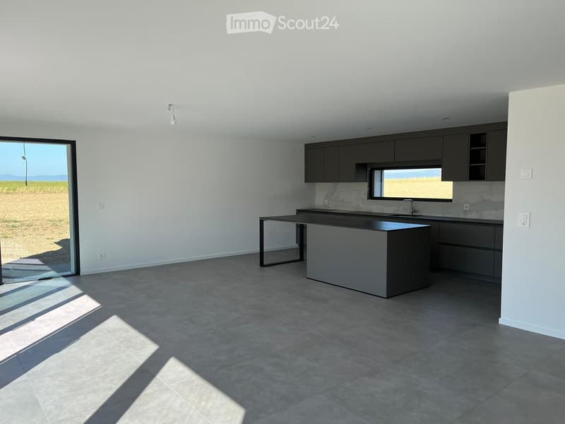 Modern kitchen with grey cabinets, a central island, and large windows overlooking a field.