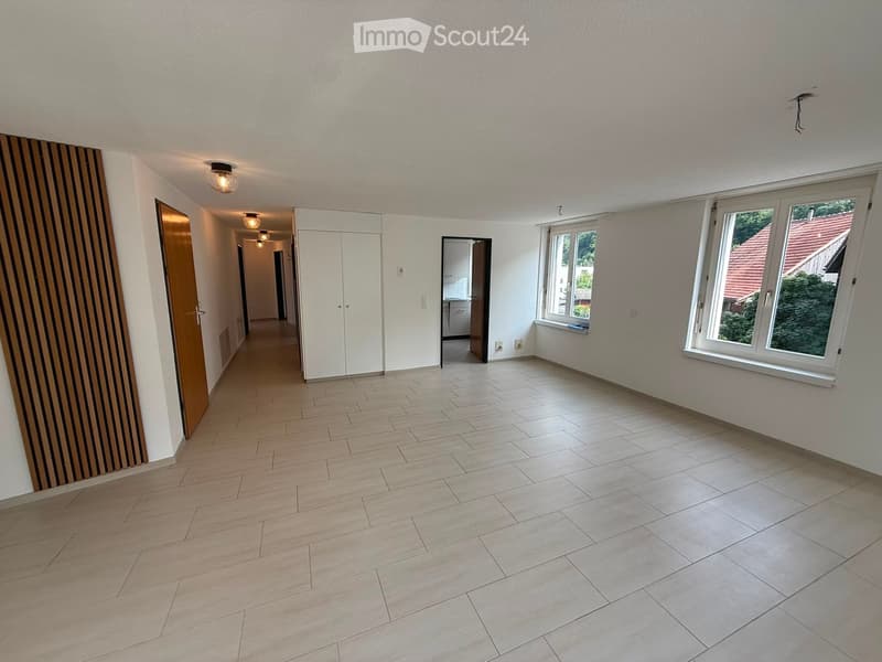 Empty room with light-colored tiled floor, white walls, large windows, and a door leading to a hallway.