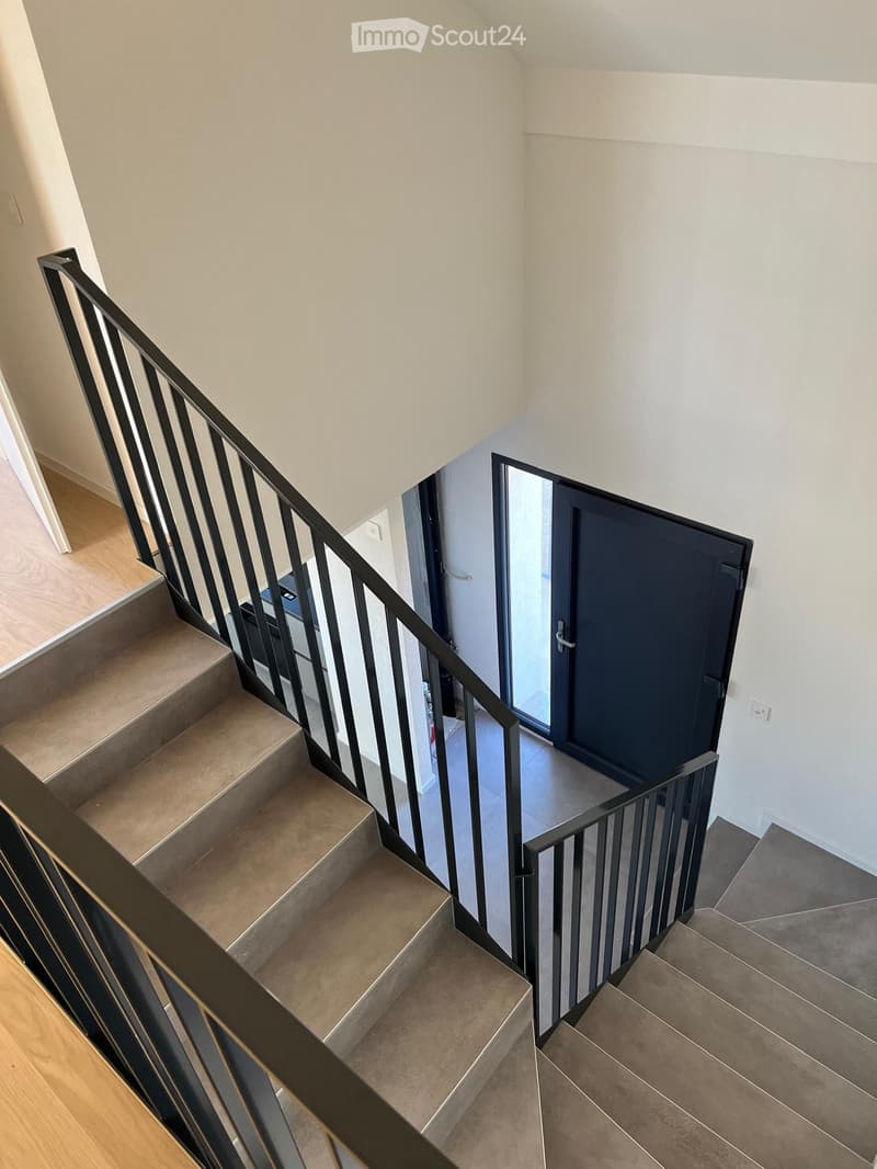 Modern staircase with beige tiled steps, black metal railing, and a glass door leading to another area.