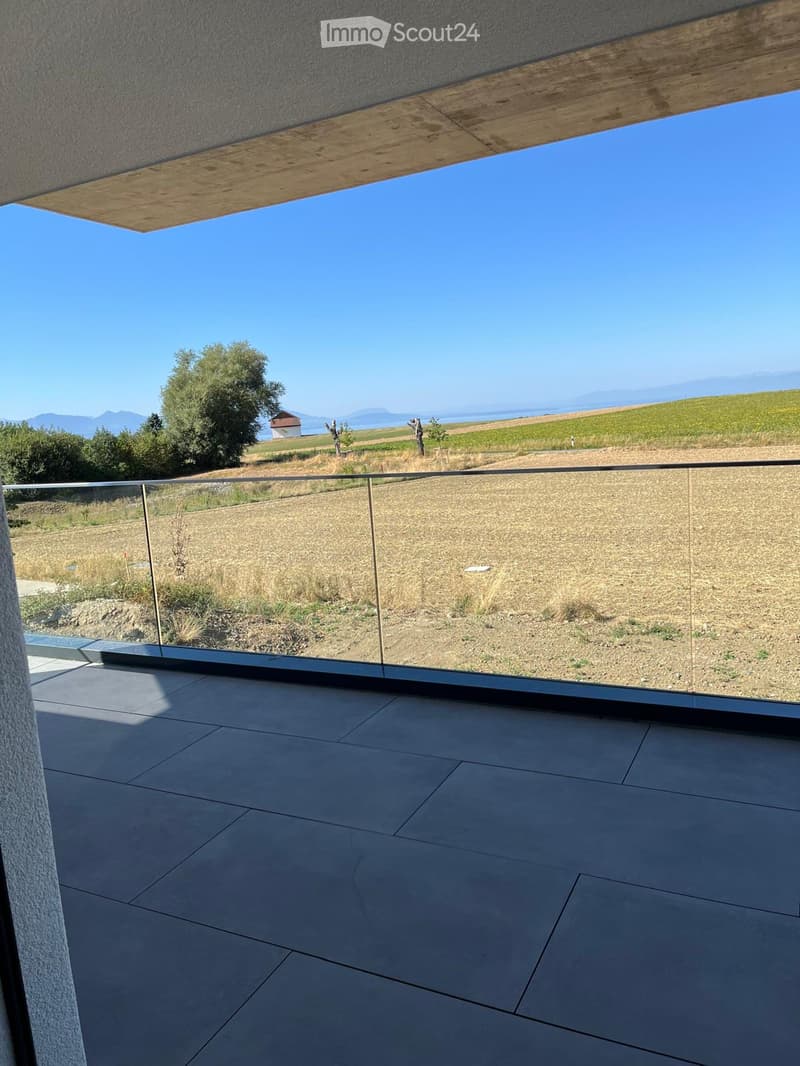Modern balcony with glass railing, tiled floor, and scenic countryside view.