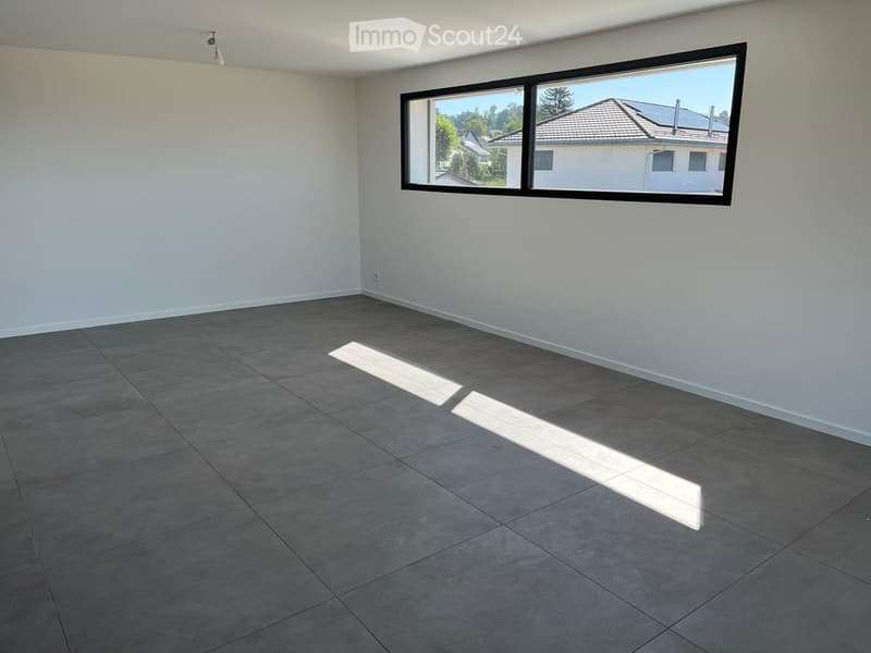 Empty room with grey tiled floor and white walls, featuring a large window with a view of neighboring houses and trees.