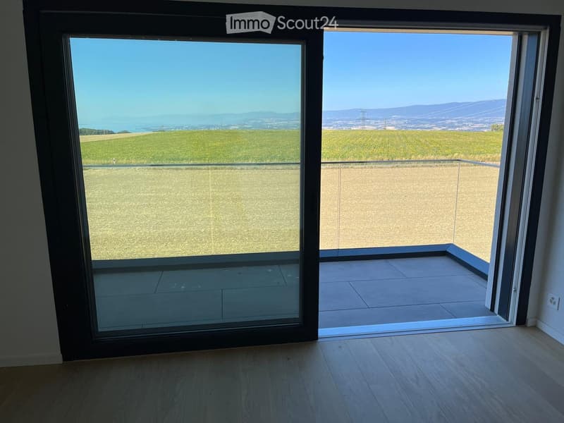 Open sliding glass doors lead to a tiled balcony with a panoramic view of fields and distant hills.